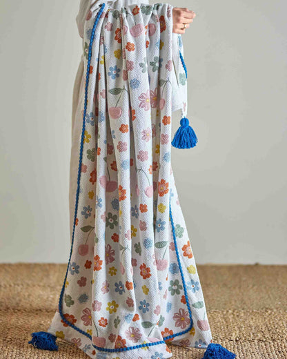 Bunte Decke mit Blumen und Kirschen und blauen Bommeln.